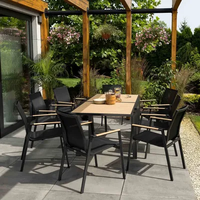 An outdoor patio dining set with a table and chairs under a wooden pergola, surrounded by lush greenery and hanging plants.
