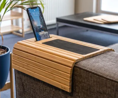 A wooden sofa armrest tray with a phone in a slot and a black insert.