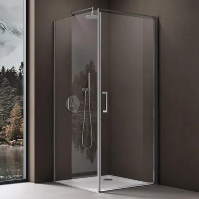 A modern shower cabin with a glass door and silver fixtures, set against a dark wall and a window showing a landscape.