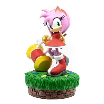 A statue of Amy Rose from Sonic the Hedgehog, holding a large hammer, standing on a grassy base with flowers.