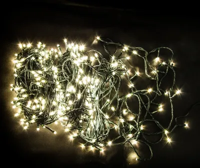 A tangled pile of white LED string lights with green wire on a dark background.