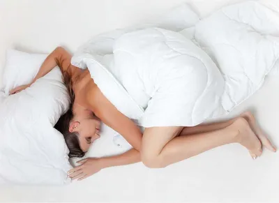 A woman is sleeping in a bed, covered by a white duvet.
