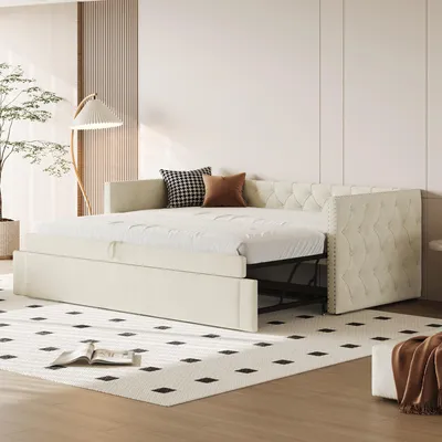 A cream-colored sofa bed is shown in a room with a modern aesthetic, featuring a large plant and a floor lamp.