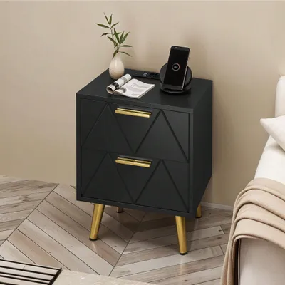A black nightstand with gold legs and handles, featuring a phone charging on a wireless charger, a magazine, and a small plant.