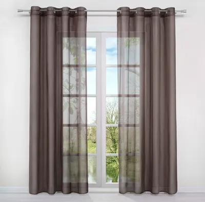 A window with brown curtains and sheer voile panels, showing a view of trees and water outside.