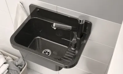 A black granite sink with a silver faucet mounted on a tiled wall.