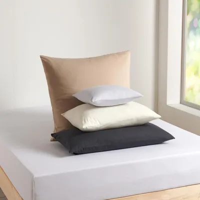 A stack of four pillows on a white bedsheet.