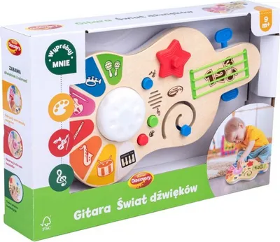 The image shows the retail packaging of a wooden guitar-shaped toy for babies, with a child playing with a similar toy in the background.