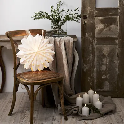 A white paper star lantern is placed on a wooden chair, with a draped cloth and candles on the floor.