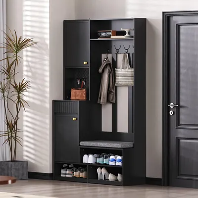 A black entryway organizer with a bench, shelves, and hooks, placed in a hallway next to a potted plant and a door.