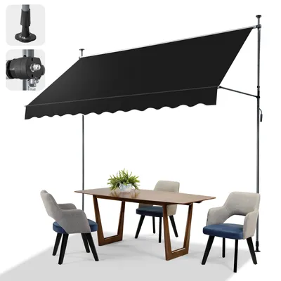A black awning is extended over a dining table and chairs on a patio or balcony.