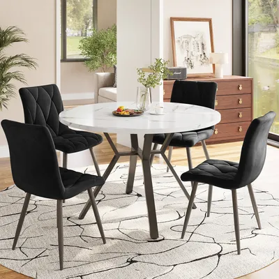 A dining set with a round white marble-top table and four black velvet chairs in a well-lit room.