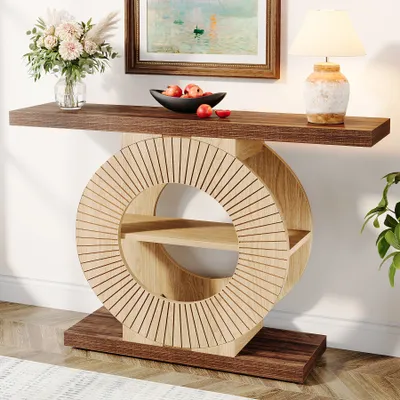 A console table with a circular shelf unit, decorated with a vase of flowers, a bowl of fruit, and a lamp.