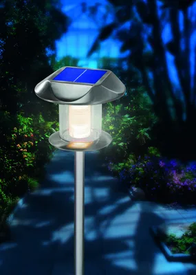 A solar garden light illuminates a pathway in a garden at dusk.