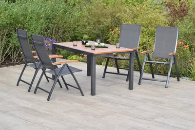 A garden furniture set consisting of a table and four chairs on a patio, with greenery in the background.