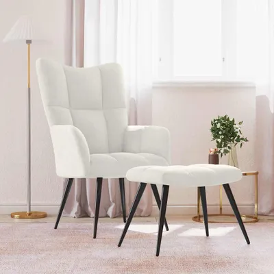 A cream-colored armchair and ottoman are placed in a room with sheer curtains and a floor lamp.