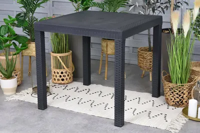 A square outdoor table is set up on a patio with plants in baskets around it.
