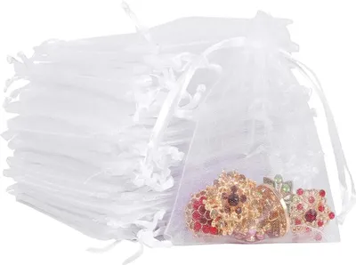 A stack of white organza bags with one bag open showing jewelry inside.