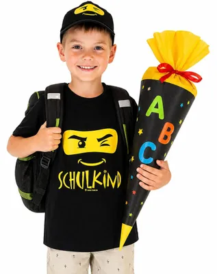 Junge mit Schulkind T Shirt und Basecap hält Zuckertüte und trägt Schulranzen zur Einschulung.