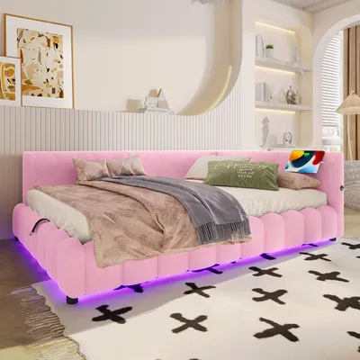 A pink upholstered daybed with LED lighting underneath, set up in a bedroom with decorative items on shelves and artwork on the wall.