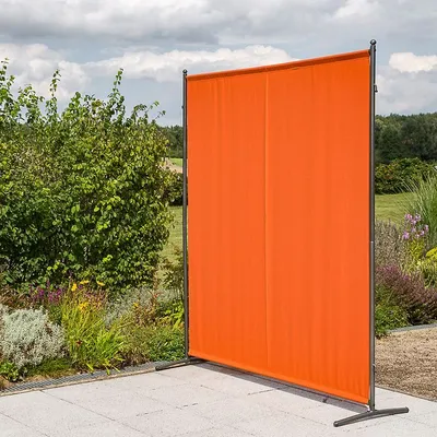 An orange privacy screen stands on a patio in a garden setting.