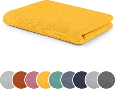 A folded yellow blanket with a waffle texture is shown on a white background. Below the blanket are circular swatches of various colors, likely representing other color options for the product.
