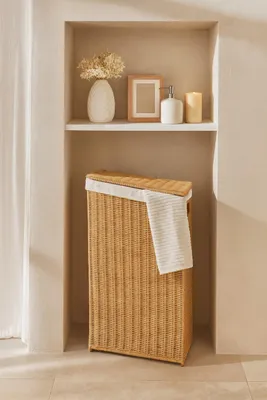 A woven laundry basket sits in a recessed shelf with decorative items on the shelf above.