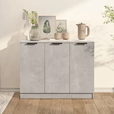 A grey sideboard with three doors is shown in a room with wooden flooring and a light-colored wall. Decorative items like plants, framed pictures, and a jug are placed on top of the sideboard.
