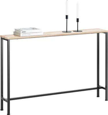 A long, narrow console table with a light wood top and black metal legs, shown against a white background. Two white candles in black holders are placed on the table, along with a stack of books.