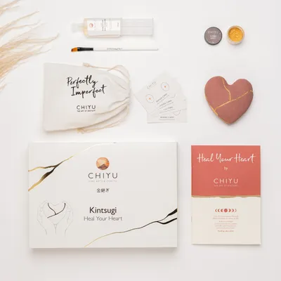 A flat lay of a Kintsugi repair kit, including a heart-shaped ceramic piece, repair materials, and instructions.
