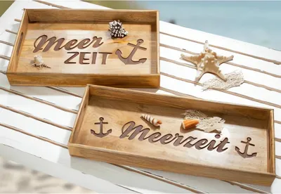 Two wooden trays with nautical-themed cutouts and decorations, placed on a white slatted surface with a beach and ocean in the background.