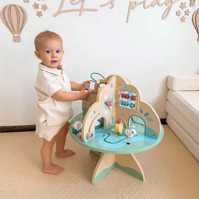 A baby is playing with a wooden activity table in a room with wall decorations.