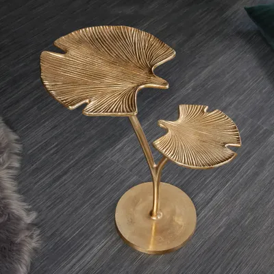A decorative golden side table shaped like ginkgo leaves on a dark grey floor.