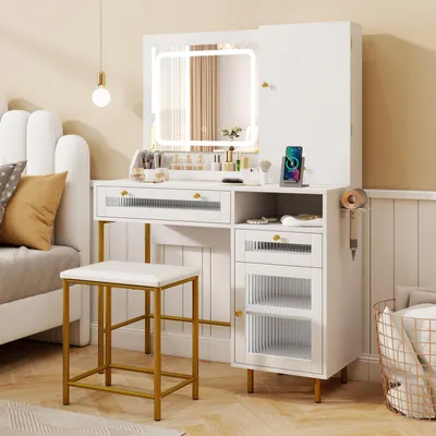 A white vanity set with a lighted mirror, stool, and storage drawers, placed next to a bed in a bedroom setting.
