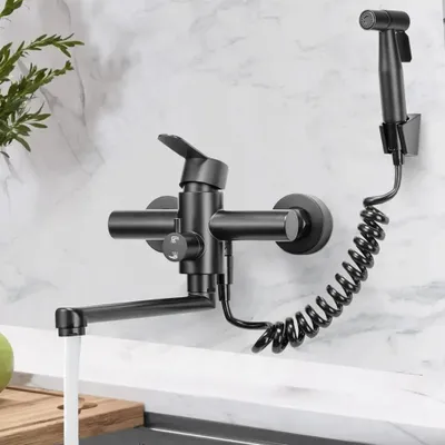 A black kitchen faucet with a sprayer is mounted on a marble-patterned wall above a countertop.