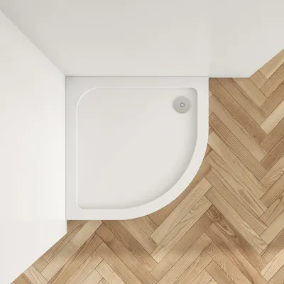 A top-down view of a white, quarter-circle shower tray placed on a herringbone wooden floor.