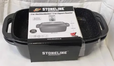 A black roasting pan with handles, partially covered by its product packaging, is placed on a white, textured surface.