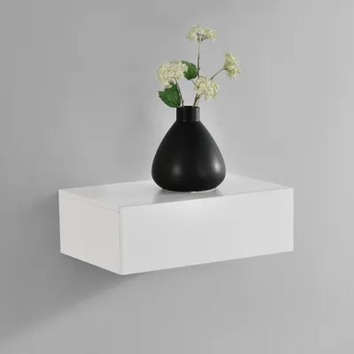 A white floating shelf with a black vase and flowers on it, against a light gray wall.