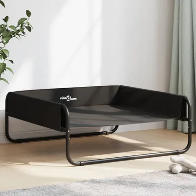 A black elevated dog bed with a steel frame is shown in a room with a plant and curtains.