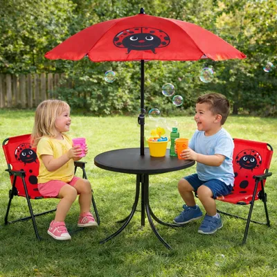 Two children are sitting at a small table with an umbrella in a backyard.