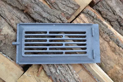 A cast iron stove grate is placed on a pile of firewood.