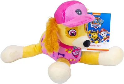 A plush toy of Skye from Paw Patrol is lying on a white background, with its packaging behind it.