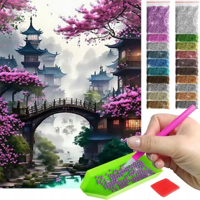 A diamond painting kit with a landscape scene and a hand holding a tool to pick up beads.
