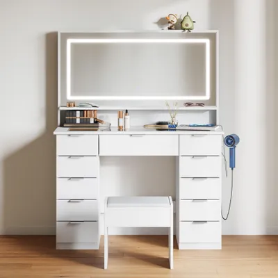 A white vanity table with a lighted mirror and a stool, set against a light gray wall.
