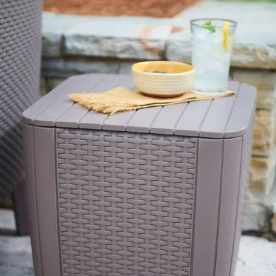 A close-up of a Keter Luzon Rattan-Optik side table with a drink and a bowl of berries on top, placed outdoors on a patio.