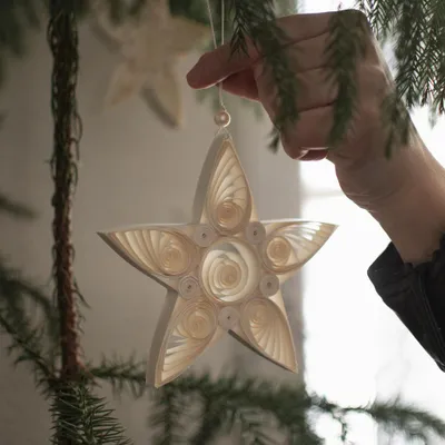 A hand holding a white paper star ornament hanging from a Christmas tree.