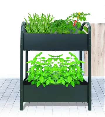A two-tiered black planter box with various green plants growing in it, placed on a tiled floor.