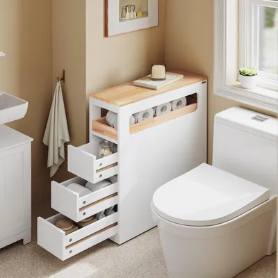A narrow bathroom cabinet with drawers and a top shelf for toilet paper is placed next to a toilet.