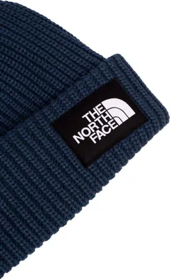 A close-up shot of a dark blue knitted beanie with a black patch featuring the white logo of 'The North Face'.