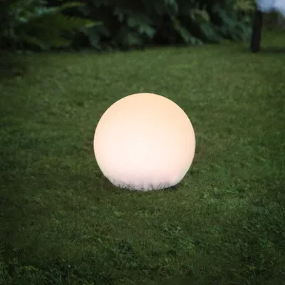 A glowing spherical light on a grassy lawn at dusk.